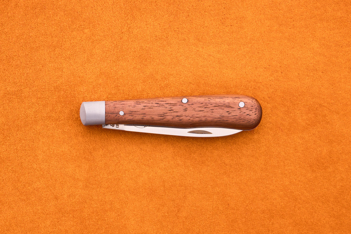 An Otter-Messer Pocket Knife Classic with a sapele wood handle and metal accents rests closed on an orange textured surface.