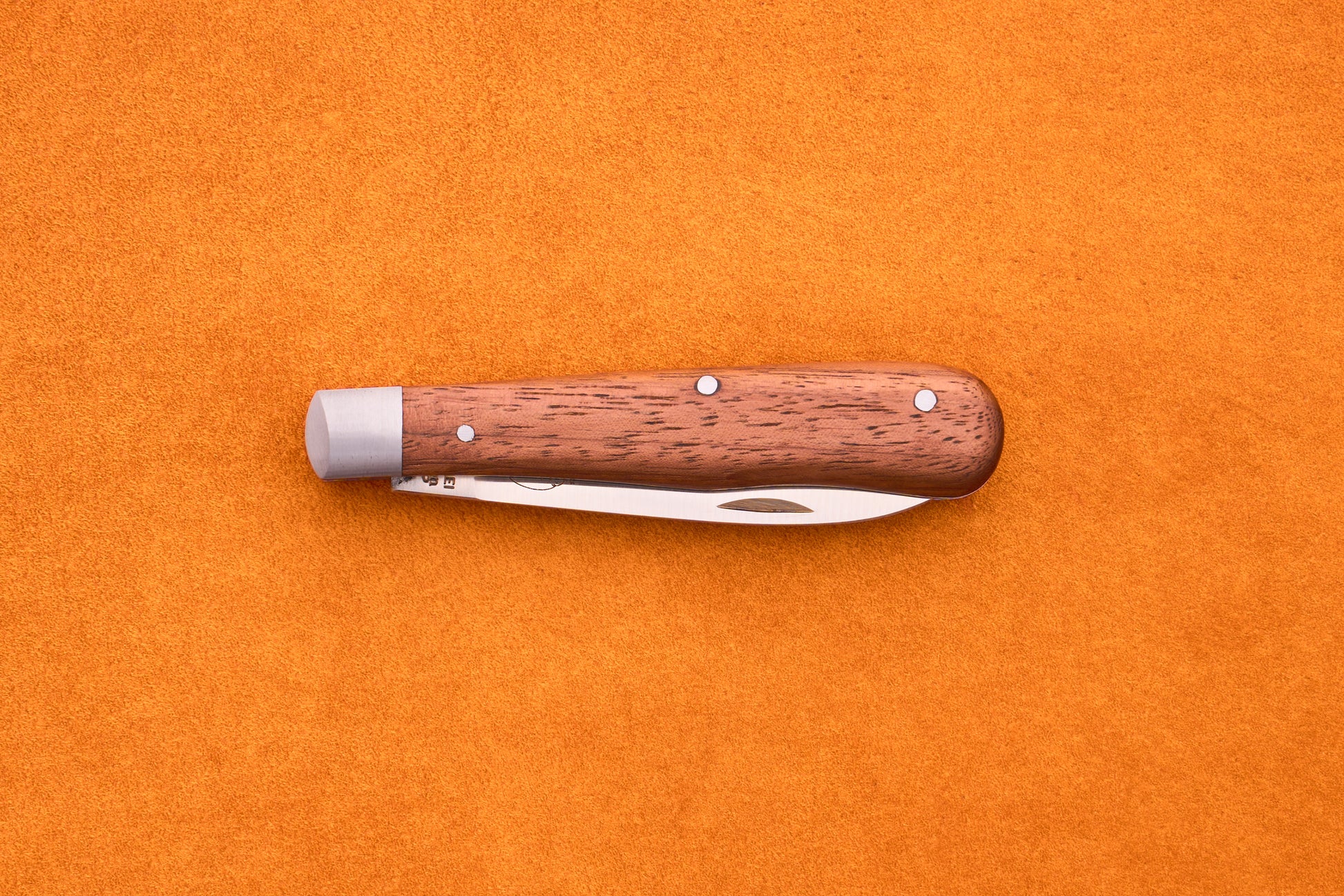 An Otter-Messer Pocket Knife Classic with a sapele wood handle and metal accents rests closed on an orange textured surface.