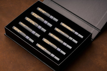 A black box containing ten 5ml perfume bottles with gold lettering, arranged in two rows on a brown surface—an elegant unisex fragrance discovery kit: the Persons of Interest Eau de Parfum Discovery Kit.