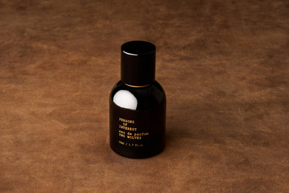 A black bottle of Persons of Interest Two Wolves Eau de Parfum rests on a brown, textured surface, suggesting the light fragrance inside—an intriguing blend of jasmine and vanilla.