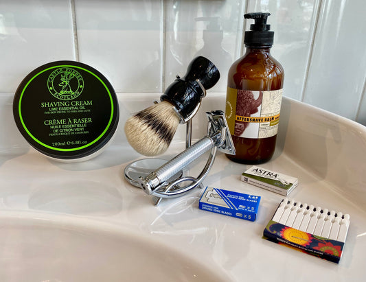 Nolan's All-In-One Shaving Kit on a washbasin, featuring a safety razor, lime shaving cream, aftershave balm, badger brush, and razor blades for classic shaving.