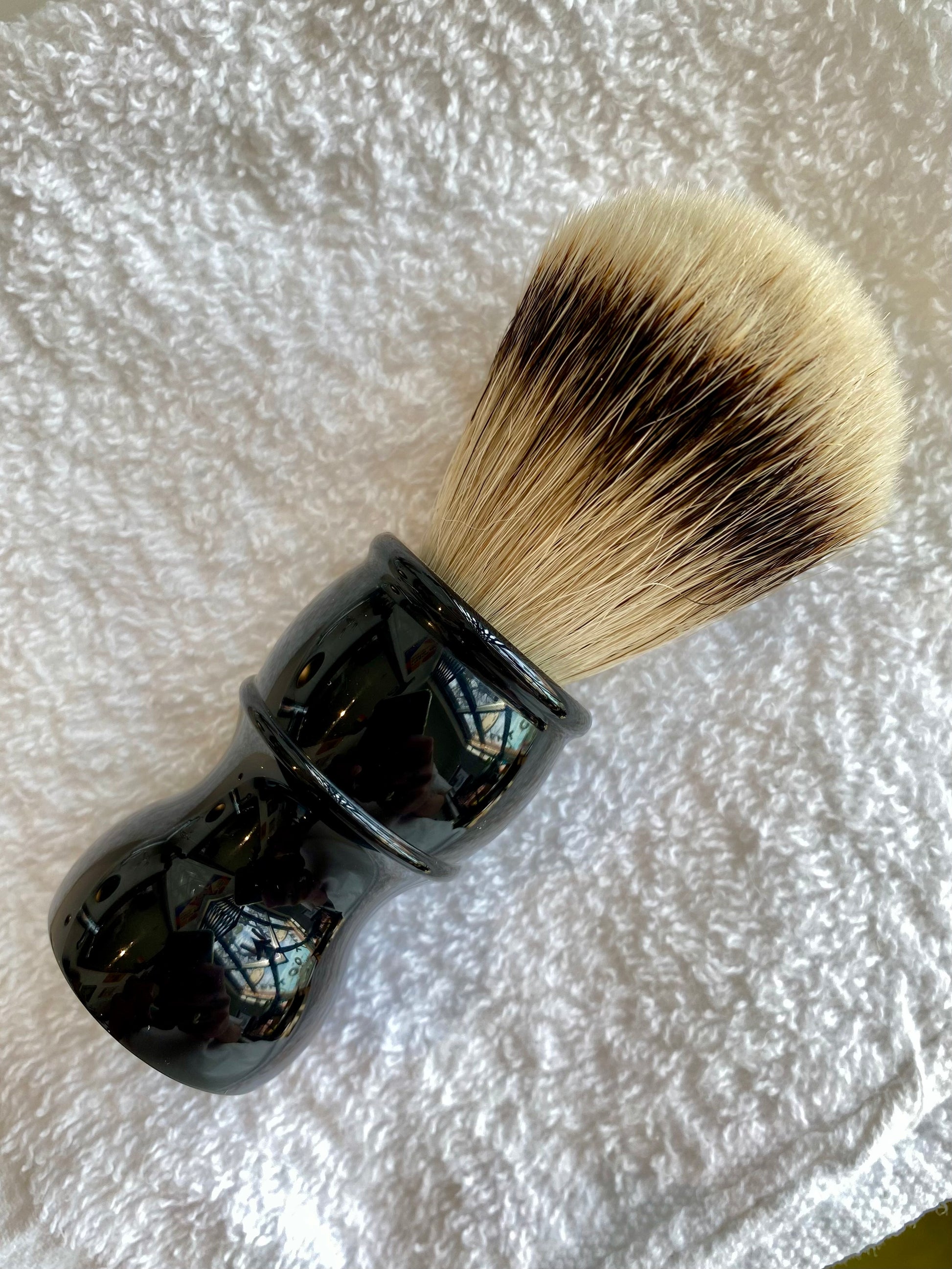 Nolan's All-In-One Shaving Kit featuring a traditional shaving brush with dense bristles and a glossy black handle rests on a white towel.