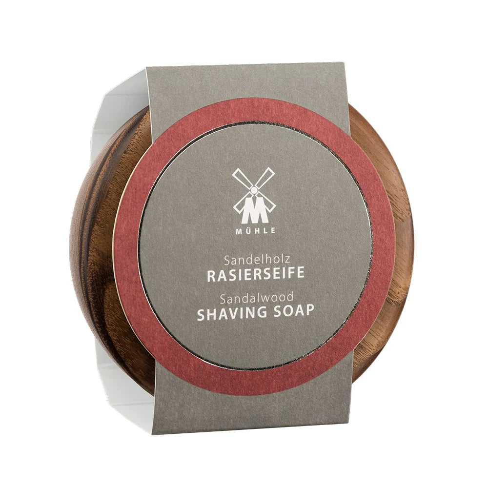 A wooden bowl holds Mühle Sandalwood Shaving Soap, which features a gray and red label displaying the product name in both German and English. Known for its luxurious sandalwood scent and exceptional lather, Mühle Sandalwood Shaving Soap is an ideal option for those looking for a classic, traditional shaving soap experience.
