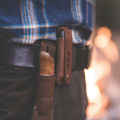 Roselli Sharpening Stone with Leather Sheath and Trigger Snap attached to a belt, alongside a knife in a sheath, evoking an outdoor, adventurous spirit.