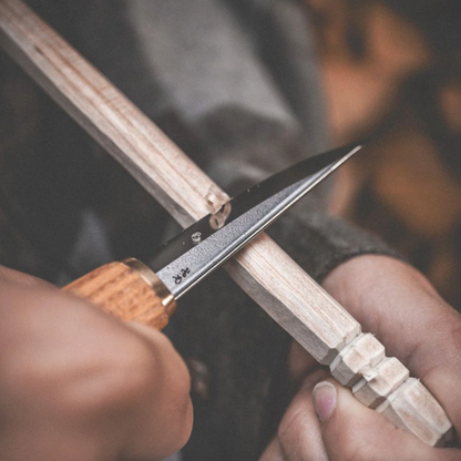 Roselli Carving Knife Short UHC in use, expertly shaping a wooden spindle, showcasing its polished scandi grind edge and dark stained curly birch handle.