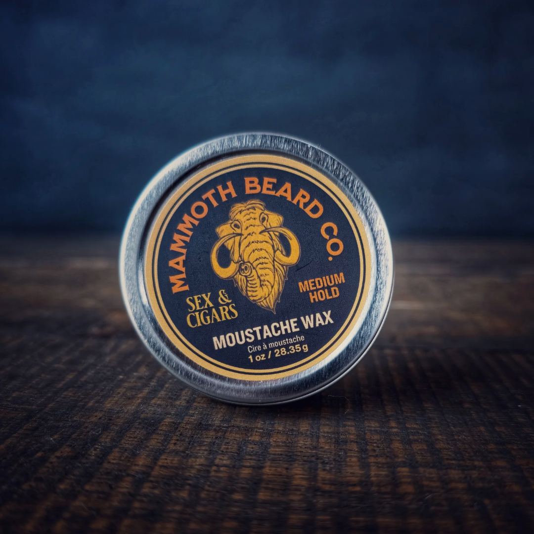 Mammoth Beard Co. Sex & Cigars Moustache Wax 1oz tin on wood surface, offering medium hold and smoky-sweet scent for versatile, casual styling.