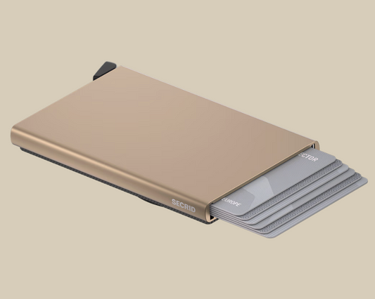 A slim, metallic gold Secrid Wallets Cardprotector for MagSafe with RFID blocking holds several partially extended gray credit cards against a beige background.