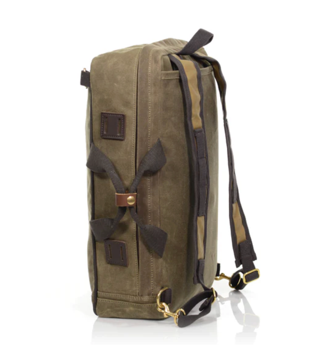Side view of an olive green Frost River Voyageur Backpack with black straps, brass hardware, and brown accents. Crafted from durable waxed canvas, this backpack stands upright on a white background.