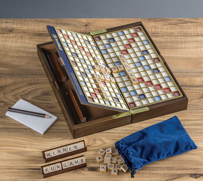 Scrabble Deluxe Travel Edition Board Game with a folding wood case, letter tiles on two racks, a notepad with a pencil, and a blue drawstring storage bag.