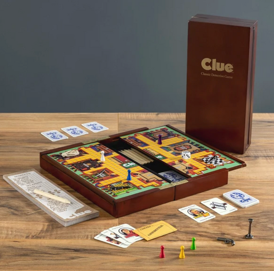 Clue Deluxe Travel Edition murder mystery game featuring a folding wooden game board, character tokens, weapon pieces, dice, playing cards, a confidential envelope, and a notepad with a pencil.