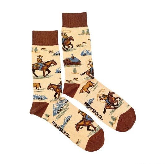 Friday Sock Co. Western Cowboy Mens crew socks in cream, featuring a repeating pattern of cowboys, barns, and mountains with brown cuffs, heels, and toes.