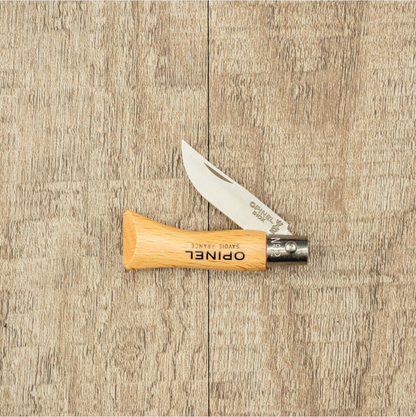 Opinel Inox No.02 Folding Knife with stainless-steel blade and beech-wood handle, partially open, showcasing timeless design on a wood-grained surface.