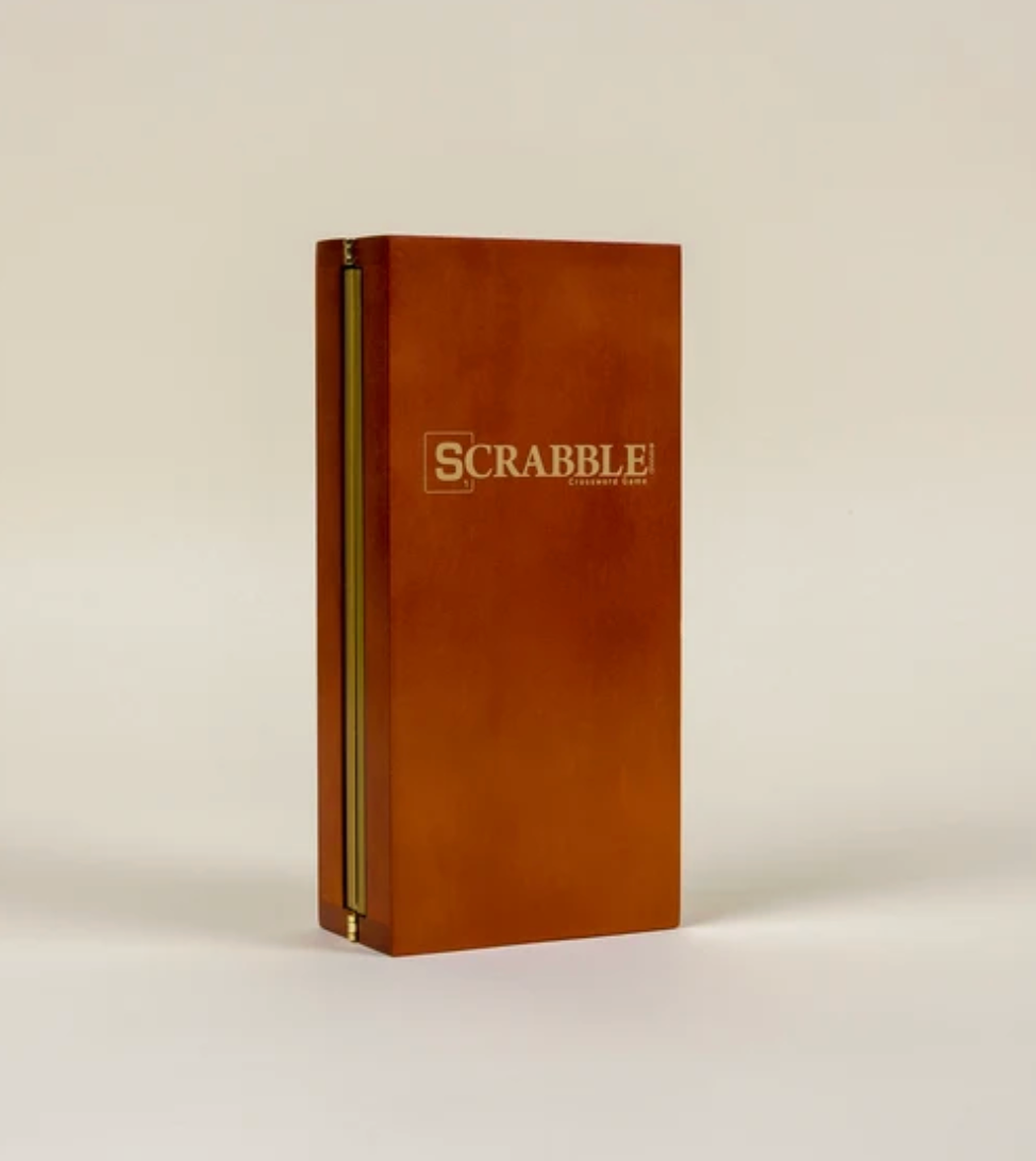 A folding wood case for the Scrabble Deluxe Travel Edition Board Game standing upright and closed, featuring the game logo on the front.