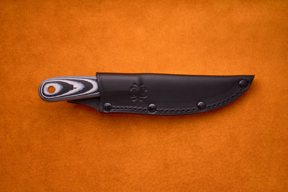 The Spyderco Bow River, featuring a black and gray handle, is partially sheathed in a black leather cover and rests on an orange surface.