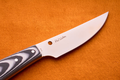 A close-up of the Spyderco Bow River bushcraft knife featuring a patterned handle and a signature engraved on the blade, placed on an orange textured surface.