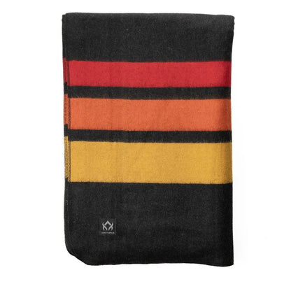 Arcturus Rainier Wool Blanket, folded with bold red, orange, and yellow stripes, featuring a small Arcturus tag, ideal for outdoor adventures and durable use.