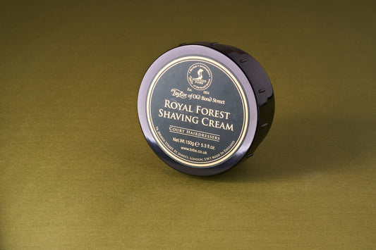 Taylor of Old Bond Street Royal Forest Shaving Cream, 150g tub, on an olive-green surface, offers a fresh, woody fragrance for a superior shaving experience.