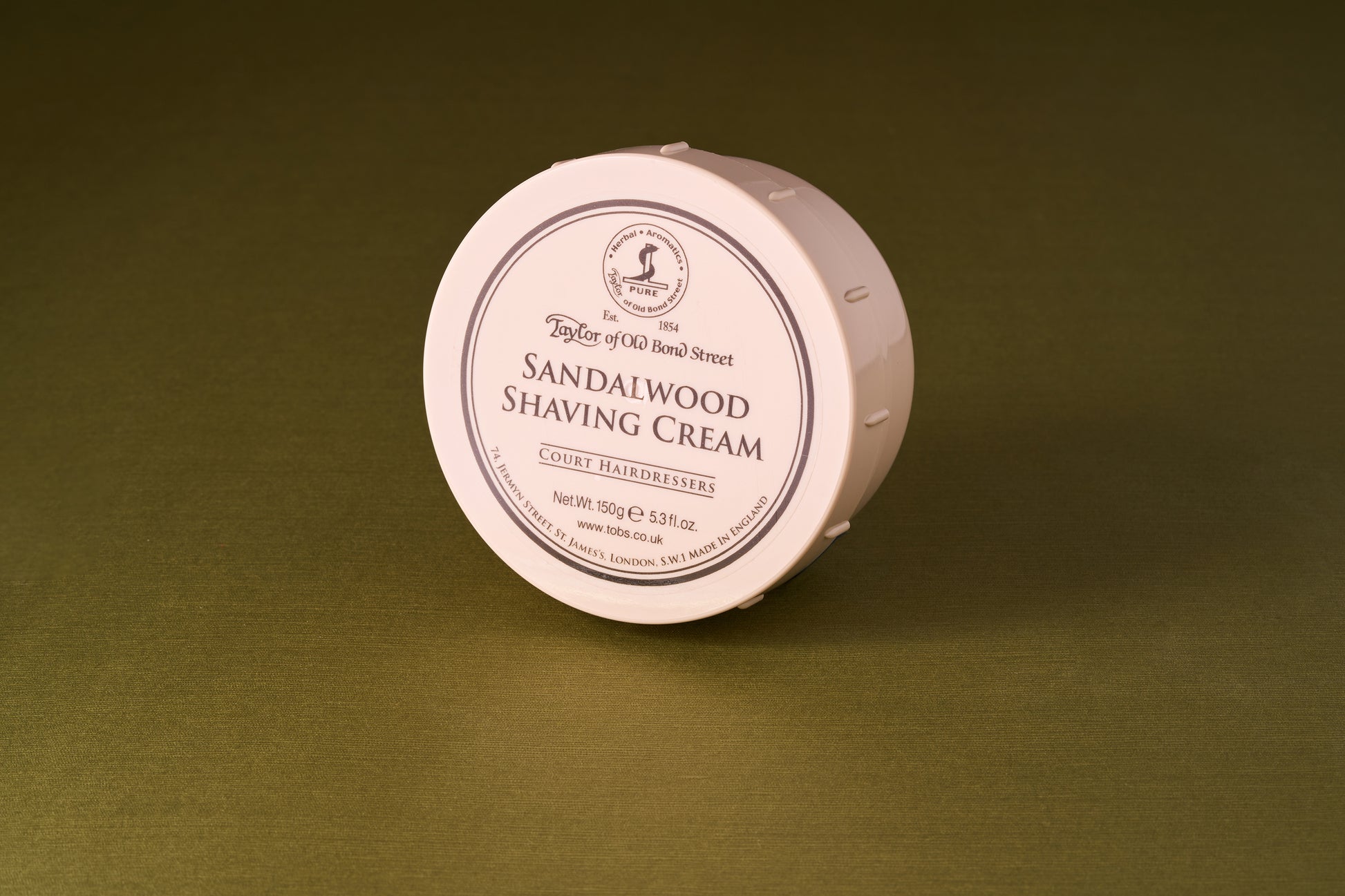 Taylor of Old Bond Street Sandalwood Shaving Cream in a 150g tub, known for its warm, woody scent and excellent lathering, displayed on an olive-green surface.