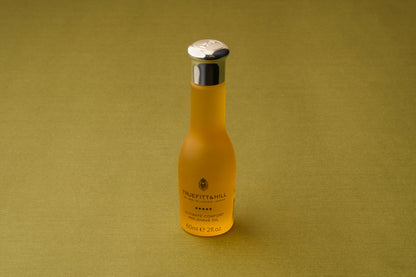 A frosted glass bottle featuring a silver cap and bearing the Truefitt & Hill Ultimate Comfort Pre-Shave Oil name (60ml), renowned as a premium men’s grooming essential, rests atop a green textured surface that recalls the refined luxury of classic Victorian shaving traditions.