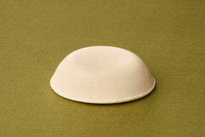 A plain, round, beige bar of Truefitt & Hill Sandalwood Luxury Shaving Soap rests on a textured olive-green surface.