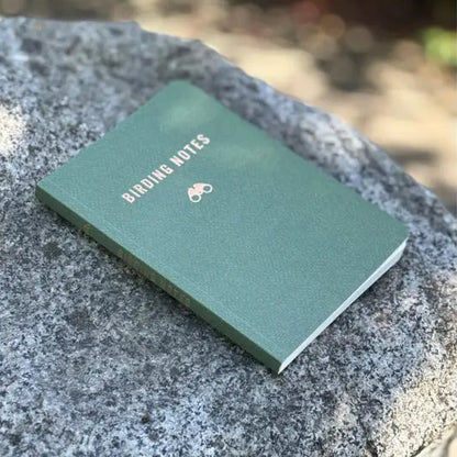 Forest-green Birding Notes notebook with embossed binoculars icon, designed for birdwatching enthusiasts, featuring prompts and a dotted graph page for sketches and observations.