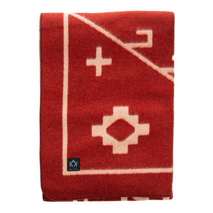 The Arcturus Rainier Wool Blanket is a folded red wool blanket featuring cream geometric patterns and a small black logo patch in the bottom corner, perfect for cozying up while camping or adding to your collection of wool blankets.