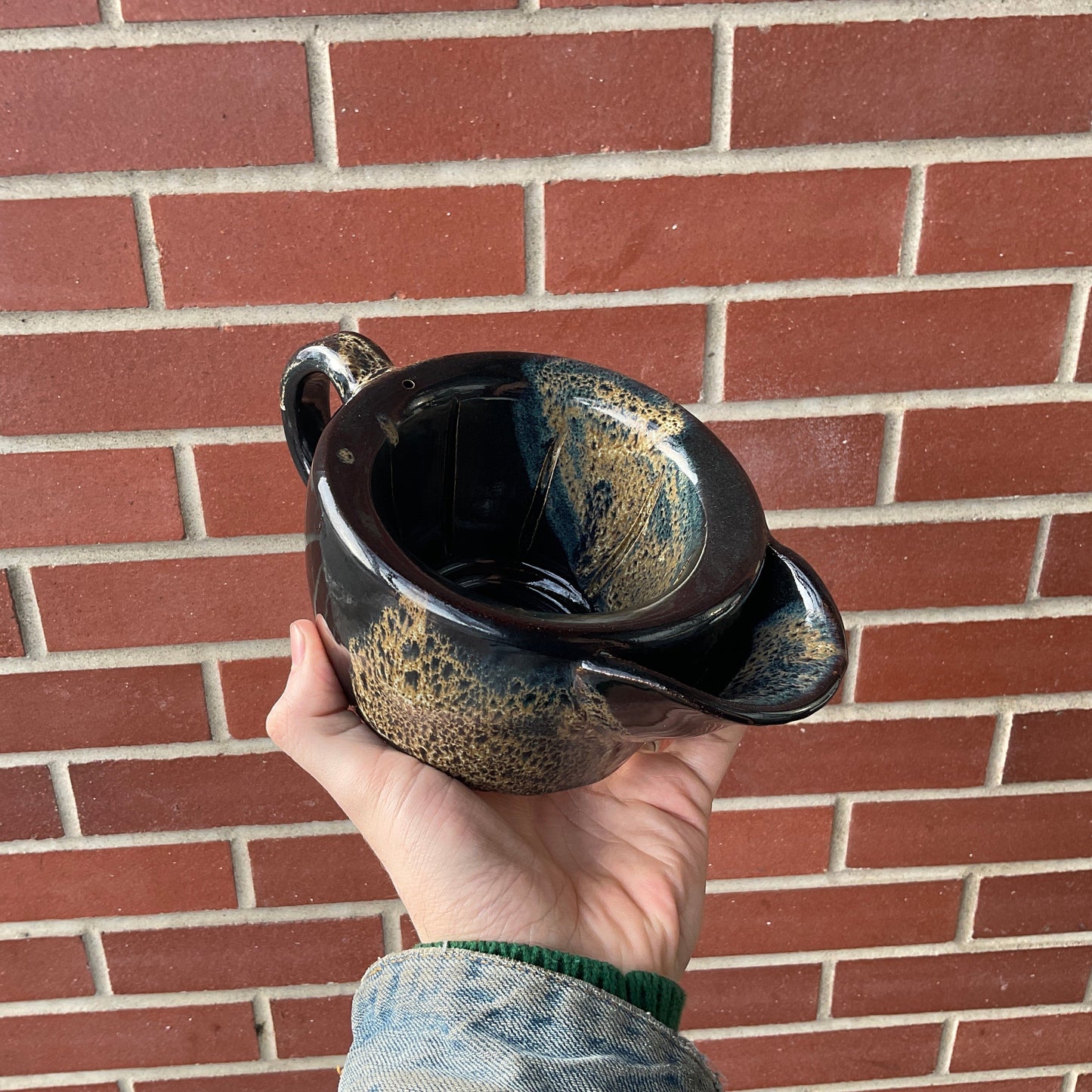 Sosan Fong Scuttle, a handcrafted ceramic pour-over coffee dripper, features distinctive ribs and spout, held against a red brick wall, highlighting its artisanal design.