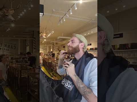 video of a man trimming his beard in the mirror with a large beard bib attached to the mirror that is catching all his hair trimmings. At the end of the video he takes the hair and throws it outside.