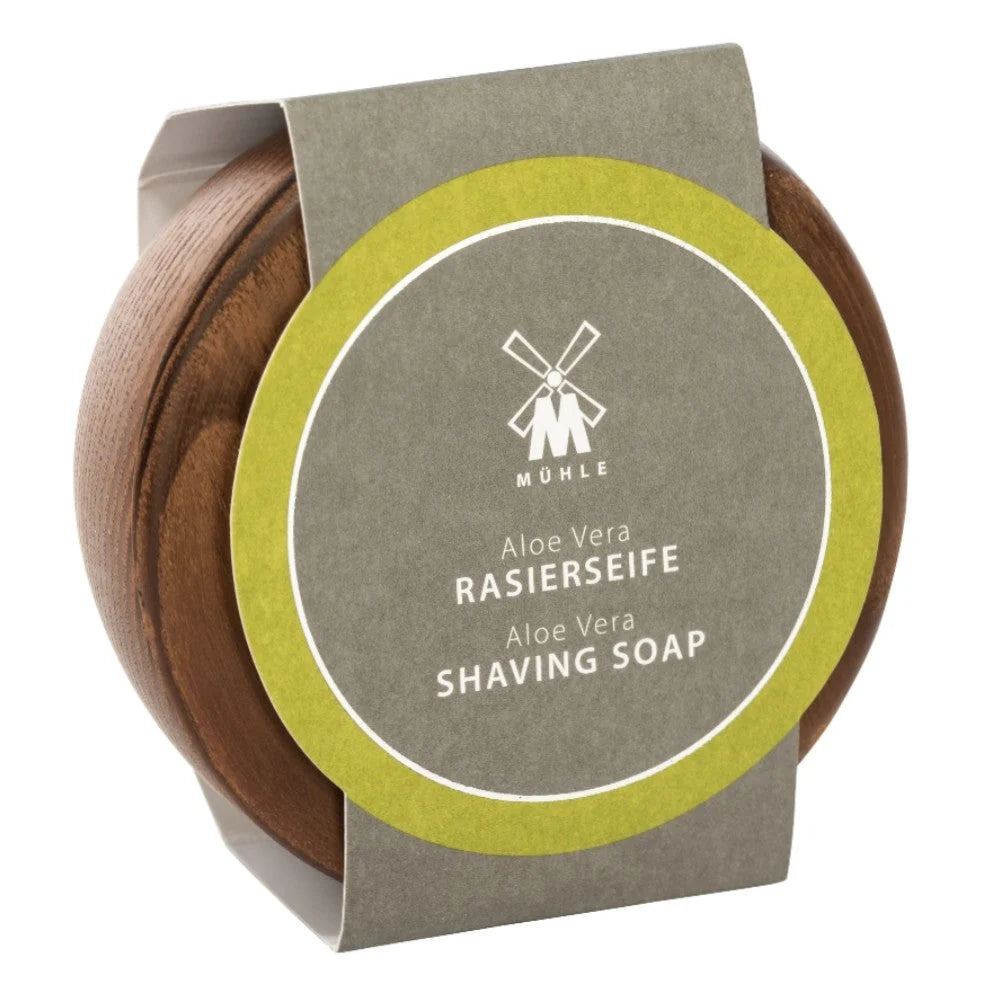 A round wooden container labeled “Mühle Aloe Vera Shaving Soap” features a green and gray design with a windmill logo. Specially formulated for sensitive skin, this Mühle shaving soap provides a gentle and soothing shaving experience.