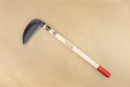 Suzuki Uchi Hamono Natakama Sickle 170mm, a hand-forged Japanese gardening tool with a curved steel blade and red-end wooden handle, ideal for cutting weeds.