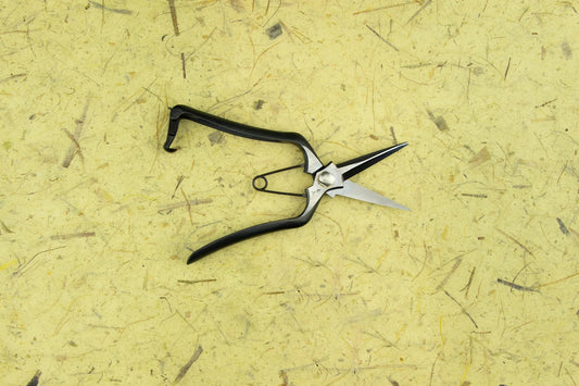 A pair of Toyama Bonsai Snips 200mm T17 with black handles lies open on a textured yellow surface, showcasing the precision craftsmanship of Japanese garden tools.
