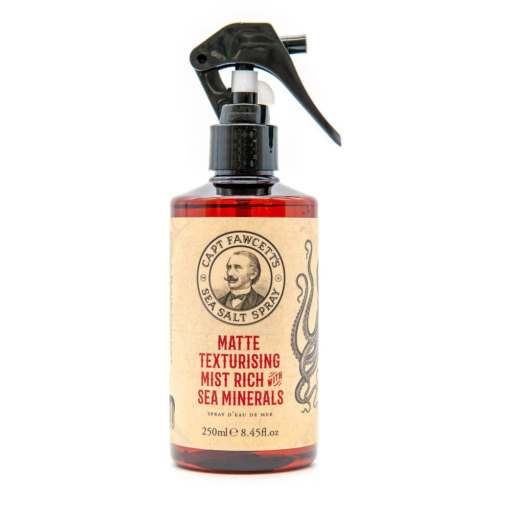 A brown bottle with a black spray nozzle labeled Captain Fawcett Sea Salt Spray, enriched with sea minerals to boost hair texture, featuring a vintage portrait and an octopus illustration.