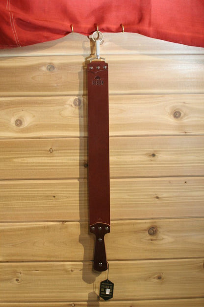 Ezra Arthur English Bridle Strop hanging on a wood-paneled wall, showcasing the Bison logo. Ideal for maintaining straight razors, emphasizing durability, and precision craftsmanship.