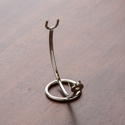 Curved Stand for Straight Razors: Chrome-plated metal stand for shaving tools, with a U-shaped fork and lower hook, elegantly storing brush and razor on a wooden surface.