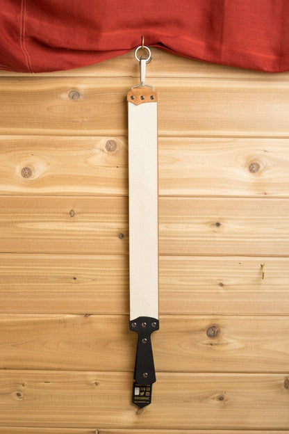 Ezra Arthur English Bridle Strop hanging on wooden wall, featuring durable leather with a handle and hook, ideal for honing straight razors efficiently.