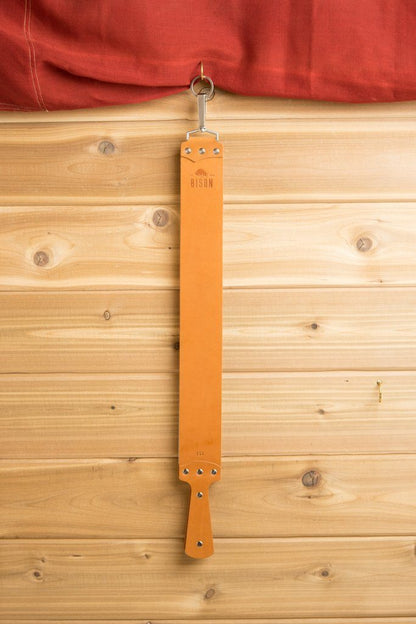 Ezra Arthur English Bridle Strop hangs from a metal hook, showcasing premium leather craftsmanship, ideal for honing razors and tools. Perfect for classic shaving enthusiasts.