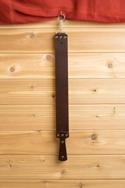Ezra Arthur English Bridle Strop hanging on wooden wall, ideal for straight razor maintenance with durable, replaceable leather, enhancing longevity and shaving quality.
