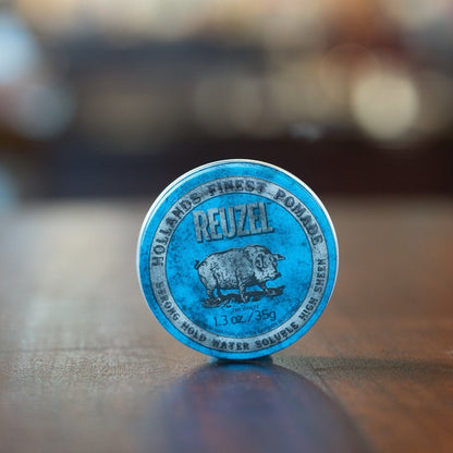 Reuzel Pomade Strong Hold Blue tin on wood surface, featuring Holland’s Finest Pomade label with pig illustration, ideal for high elevation styles and easy washout.