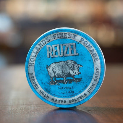 Reuzel Pomade Strong Hold Blue tin with a pig illustration, offering high hold and shine for all hair lengths, scented with vanilla wood fragrance.