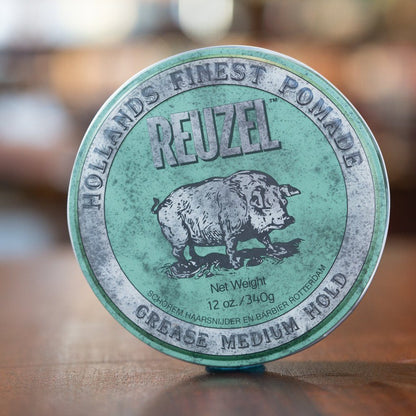 Reuzel Grease Medium Green pomade tin on wood surface, featuring a vintage pig illustration and text detailing its medium hold and shine.