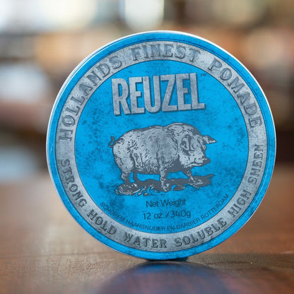 Reuzel Pomade Strong Hold Blue tin, featuring a pig illustration, offers high hold and shine for all hair lengths, ideal for tall pompadours and messy wet looks.