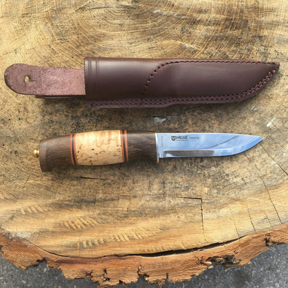Helle Knives Harding 100mm Hunting Knife with laminated wood handle and leather sheath displayed on a tree stump, showcasing traditional Scandinavian craftsmanship for precise, secure outdoor use.