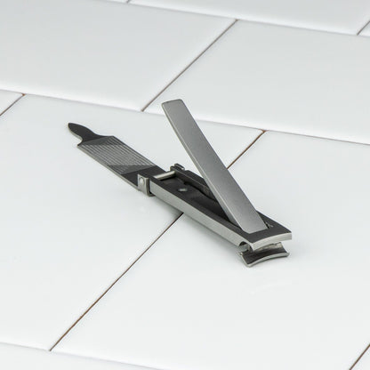 Niegeloh Inox High Carbon Stainless Steel Nail Clipper in Matte, featuring a flipped-up lever and attached nail file, rests on a white tiled surface.