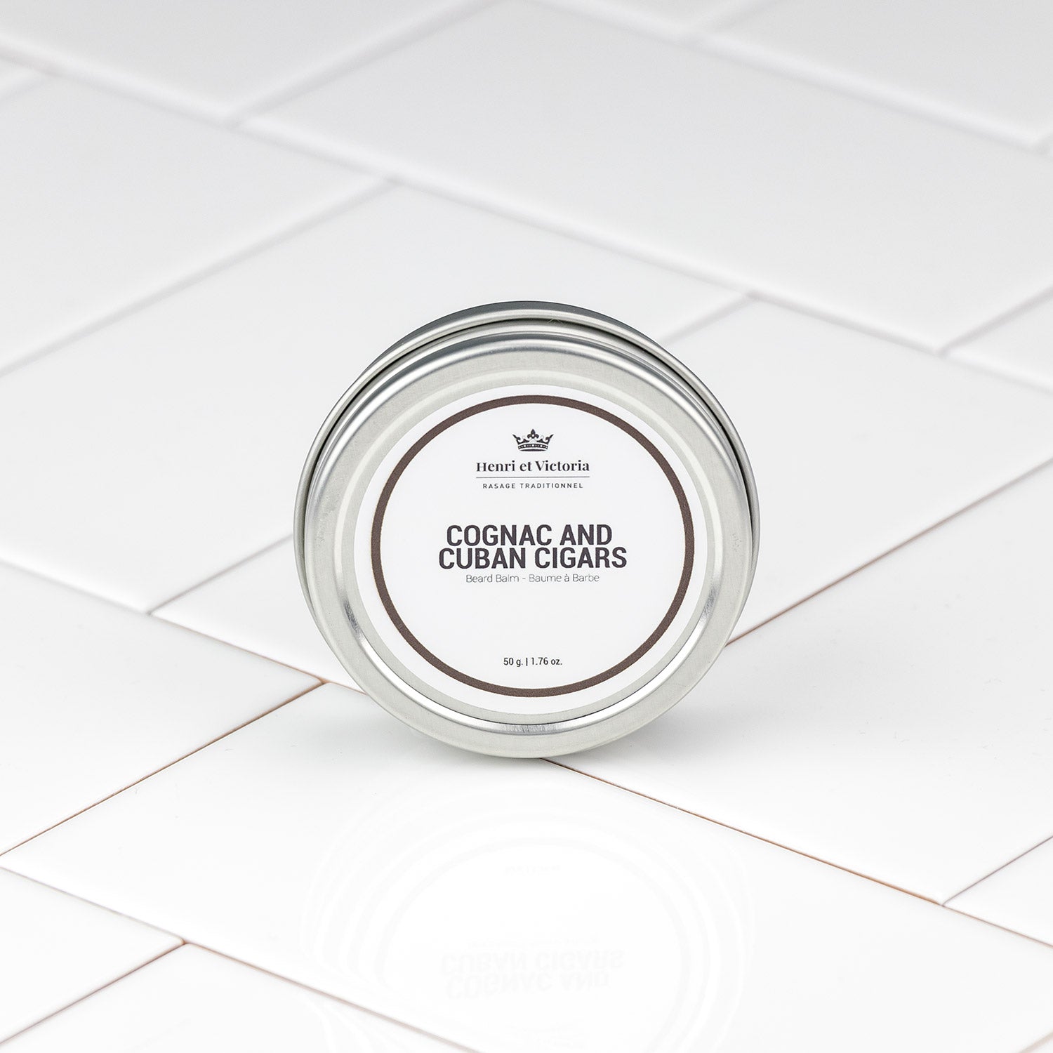 Henri et Victoria Cognac and Cuban Cigars Beard Balm in a 50g tin, offering hydration and light hold, on a glossy white tiled surface.