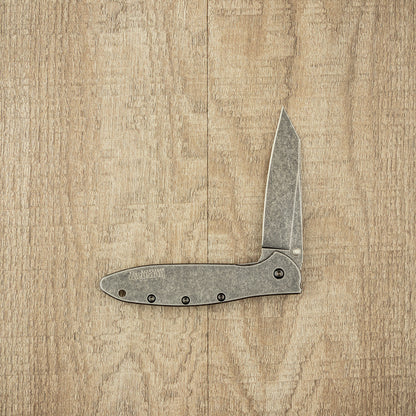 Kershaw Random Leek Blackwash knife partially open on wood surface, showcasing its crisp, sharp blade and sturdy handle for reliable everyday use.