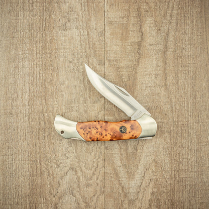 Boker Optima Thuja folding pocket knife with stainless-steel blade and polished burl-wood handle, ideal for outdoor use, shown on wooden surface.