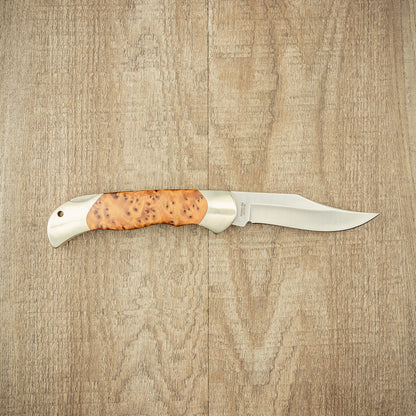 Boker Optima Thuja folding knife on wood, showcasing a polished steel blade and contoured burl wood handle with metal bolsters for versatile outdoor use.
