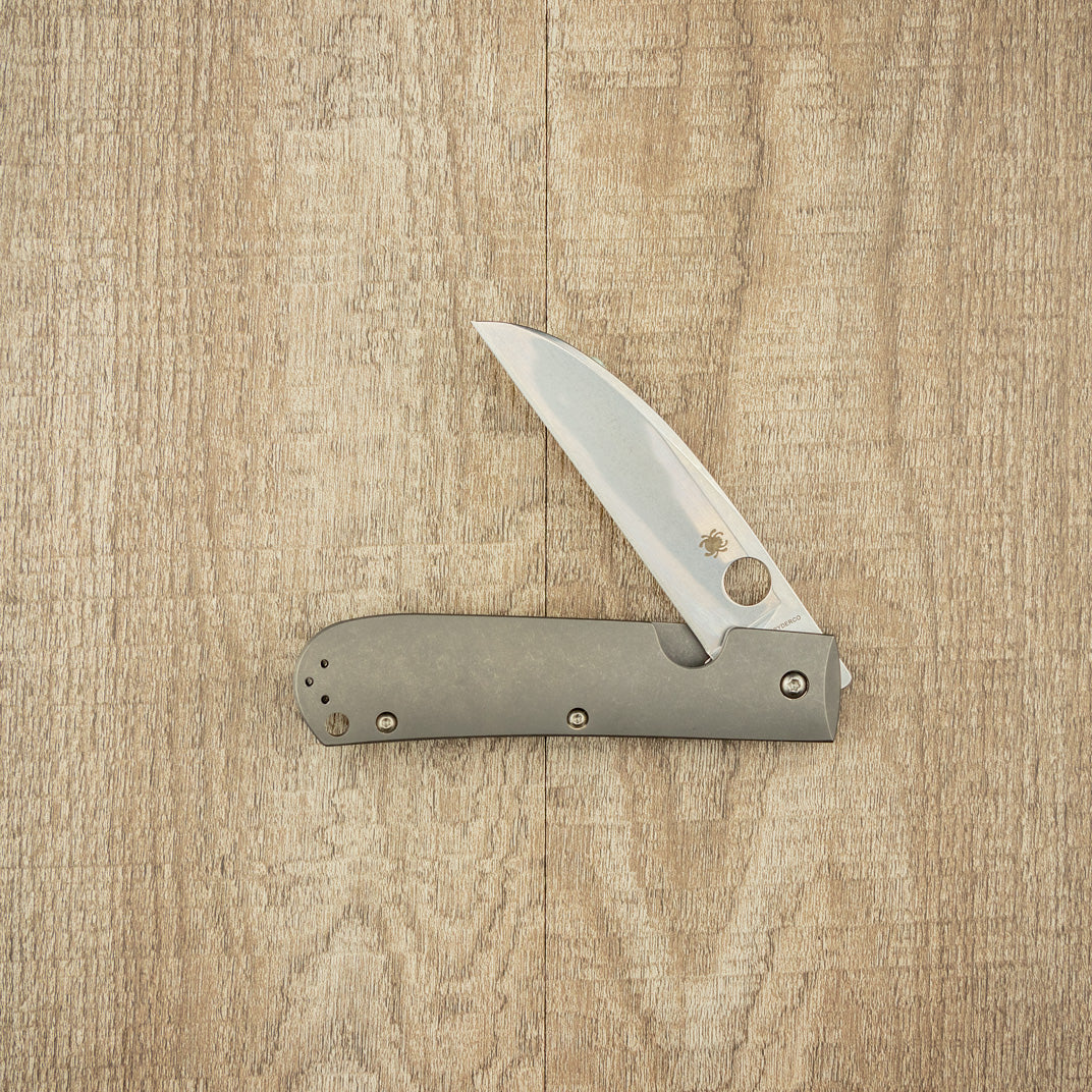 Spyderco Swayback Pocket Knife with satin-finished stainless steel Wharncliffe blade and titanium handle, featuring the iconic round thumb-hole and spider logo.