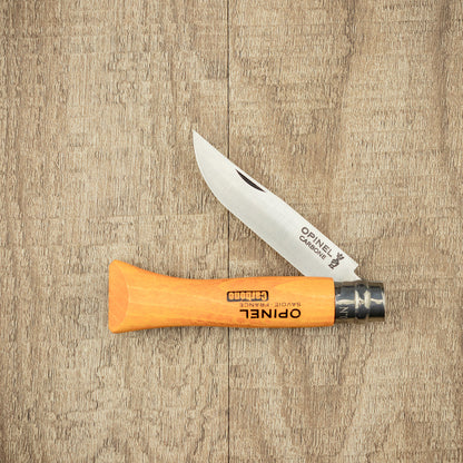 Opinel Carbon No.06 Folding Knife with a high-carbon steel blade and varnished beechwood handle, open on a wood-grain tabletop, showcasing its timeless design.