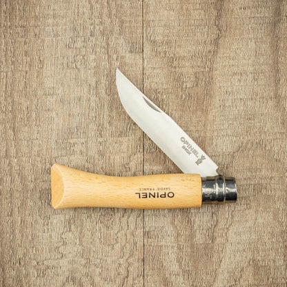 Opinel Inox No.07 Folding Knife with partly open stainless blade and beech wood handle, stamped with OPINEL SAVOIE FRANCE, on a wooden surface.